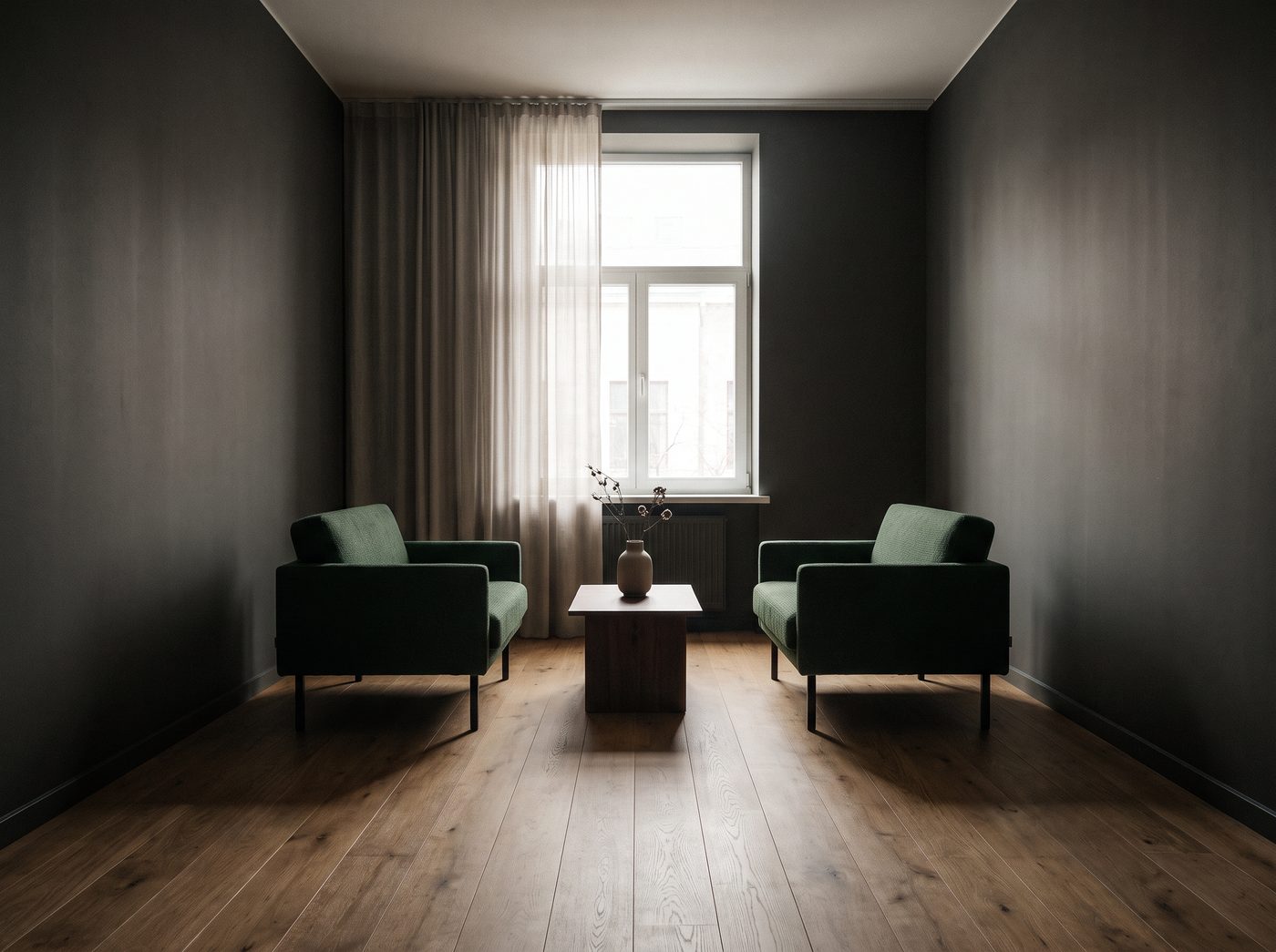 Two armchairs facing each other across a low table in a quiet, dark-walled room